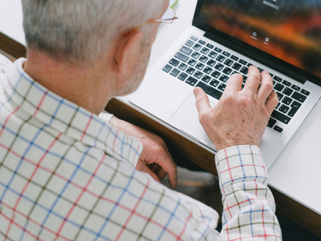 Älterer Mann, der am Laptop sitzt